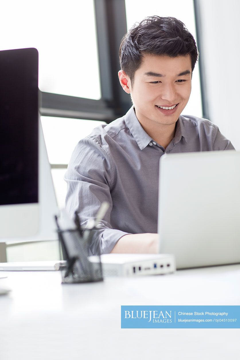 Young Chinese businessman using laptop in office