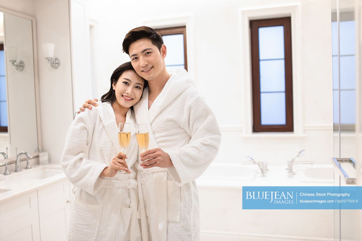 Happy young Chinese couple drinking champagne in bathroom