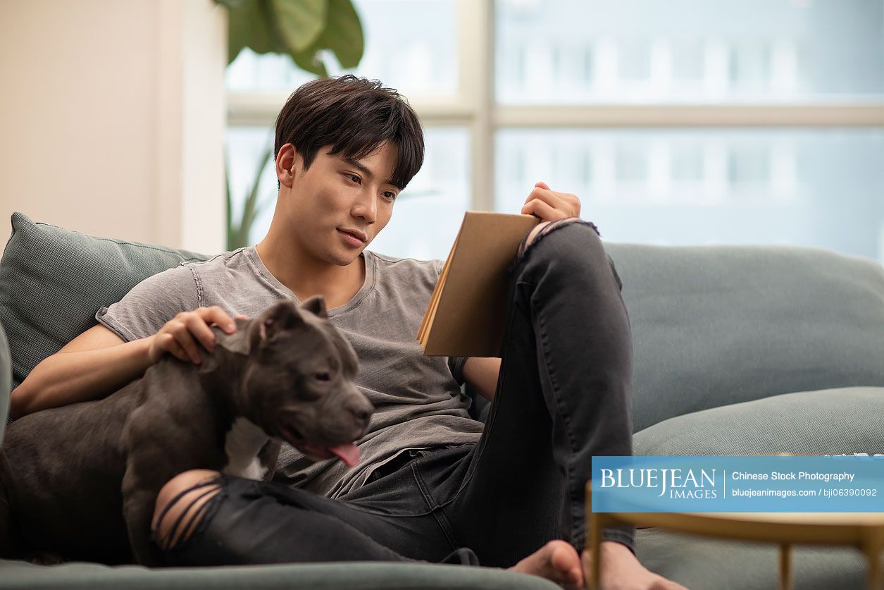 Young Chinese man with pet dog on sofa