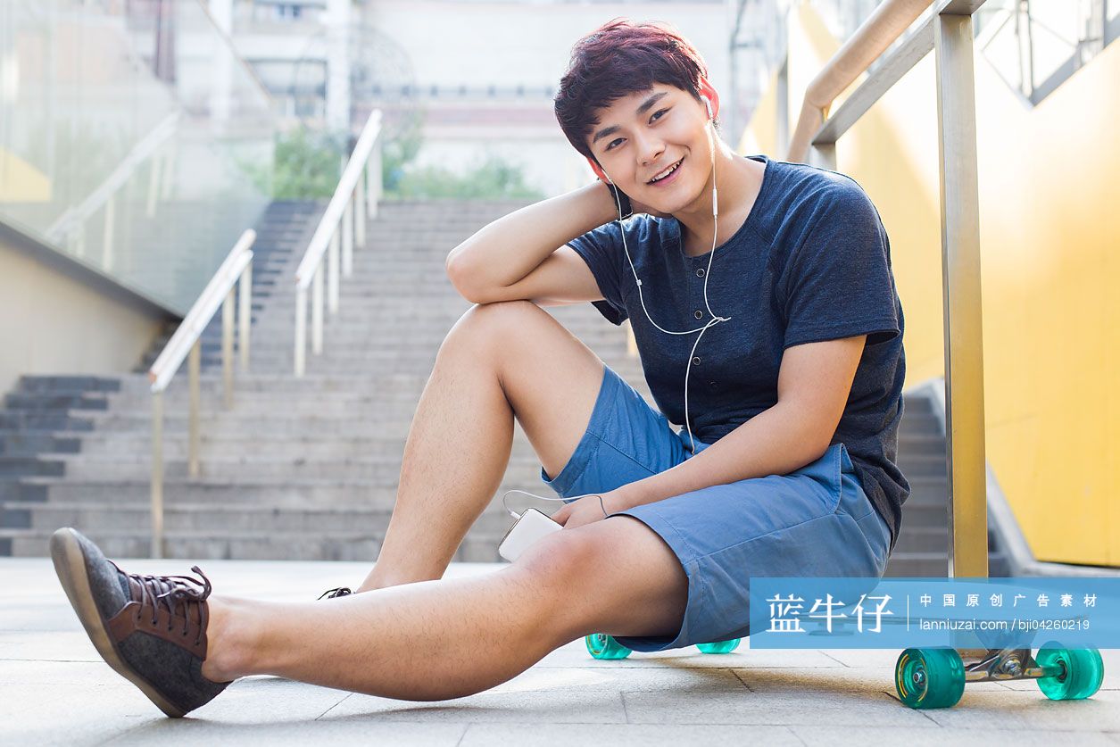 年轻男子坐在滑板上听音乐