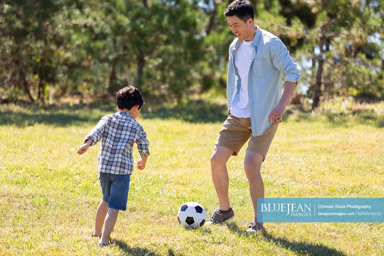 Happy Chinese father and son playing football in park