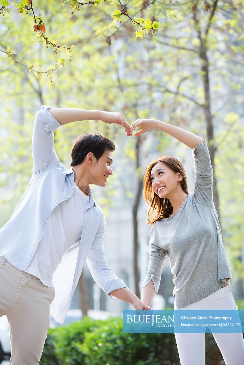 Happy young Chinese couple doing heart shape gesture