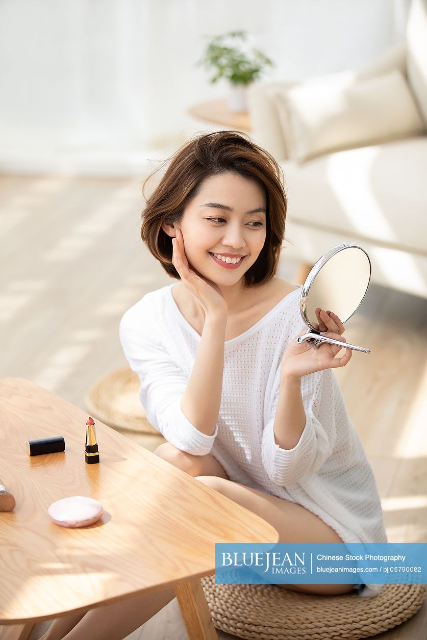 Young Chinese woman applying makeup at home