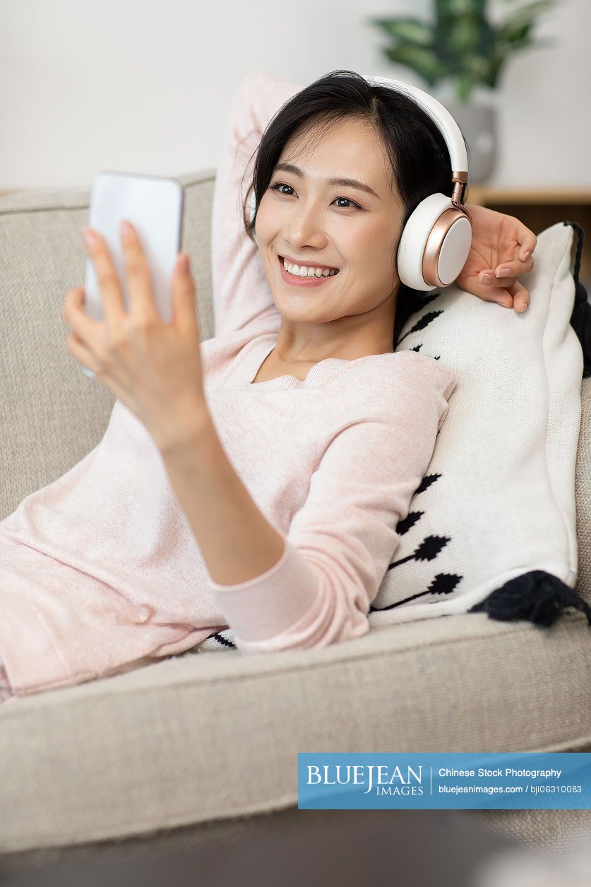 Happy young Chinese woman wearing headphones on sofa