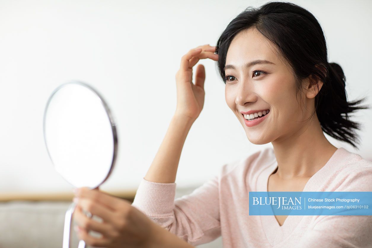 Happy young Chinese woman looking into the mirror at home