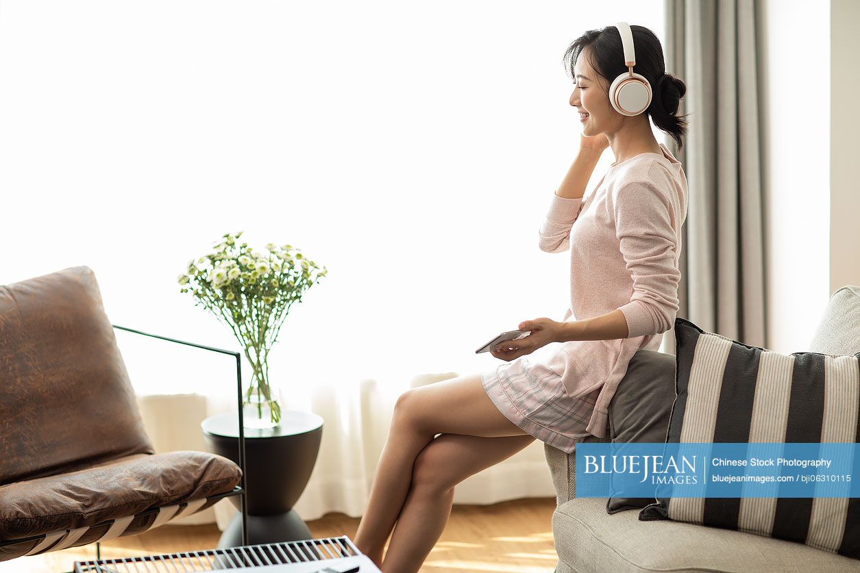 Happy young Chinese woman listening to music in living room