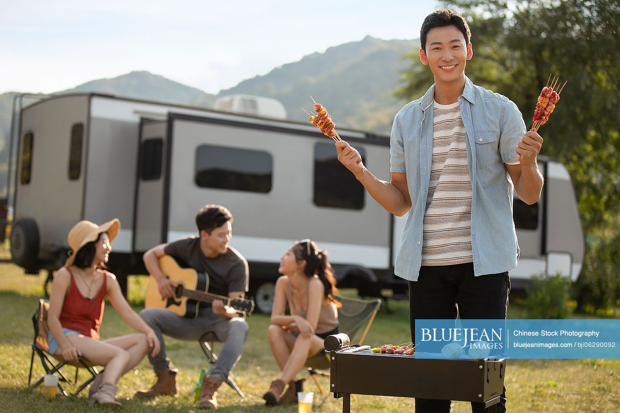 Happy young Chinese friends barbecuing outdoors