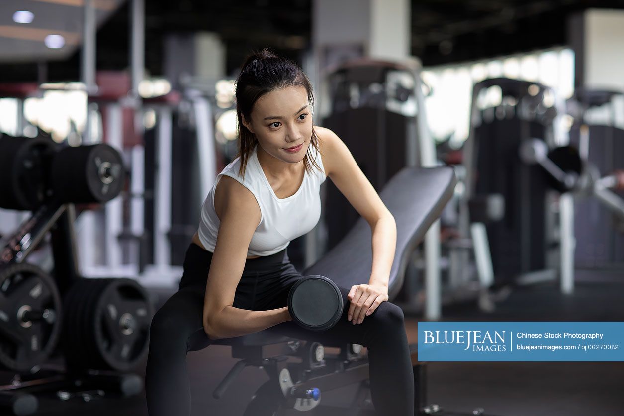 Young Chinese woman working out with dumbbell at gym