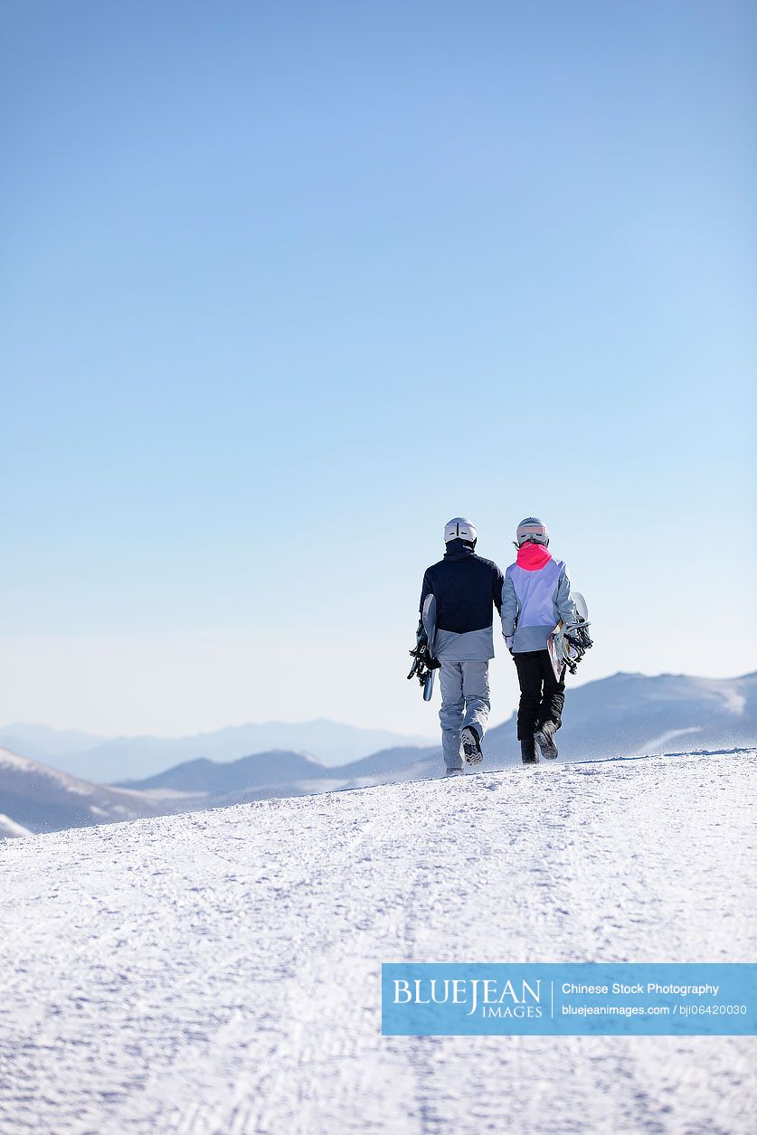 Young Chinese couple walking with snowboards on the snow