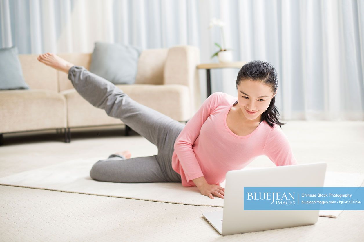 Young Chinese woman practicing yoga with laptop in living room