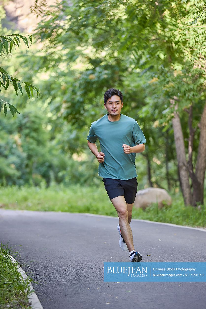 Man jogging along a road surrounded by lush trees