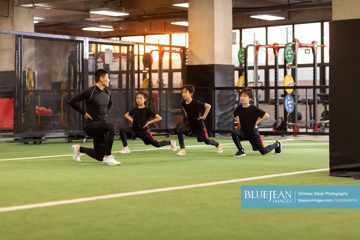 Active Chinese children having exercise class with their coach in gym