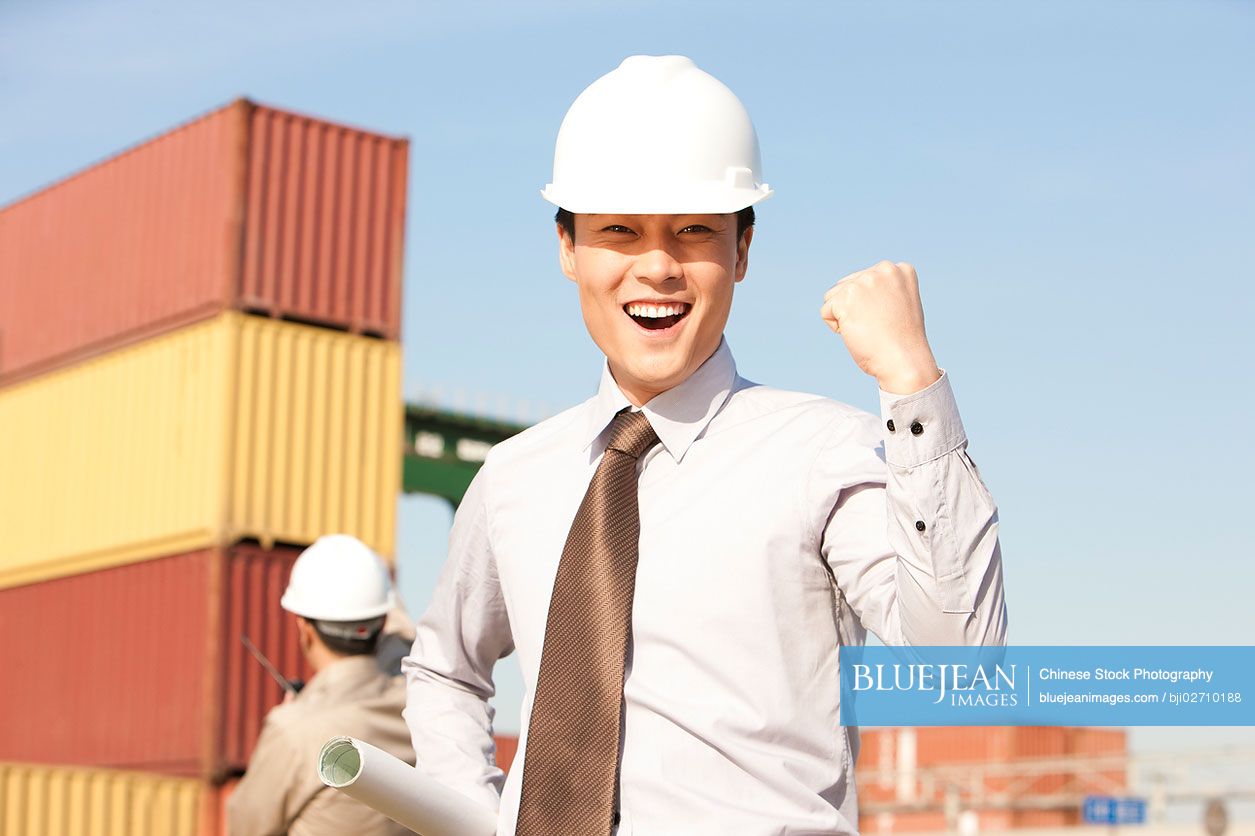 Chinese businessman with raised fist with cargo containers in the background