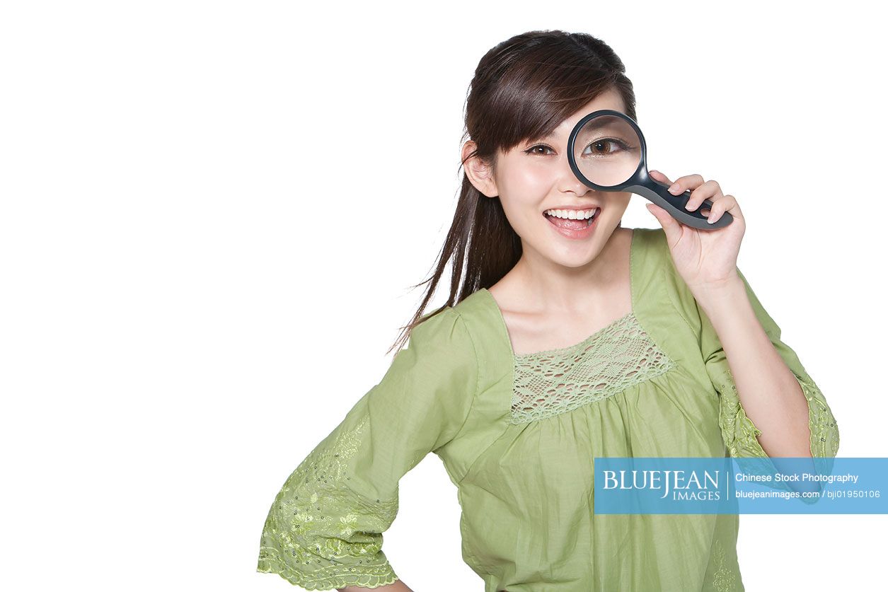 Portrait of young Chinese woman looking through magnifying glass