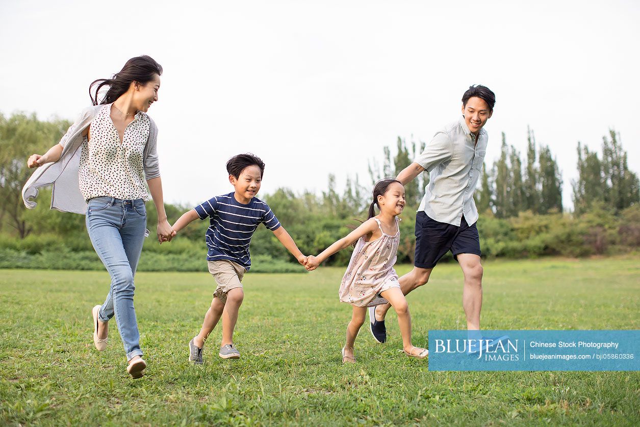 Happy young Chinese family running on grass