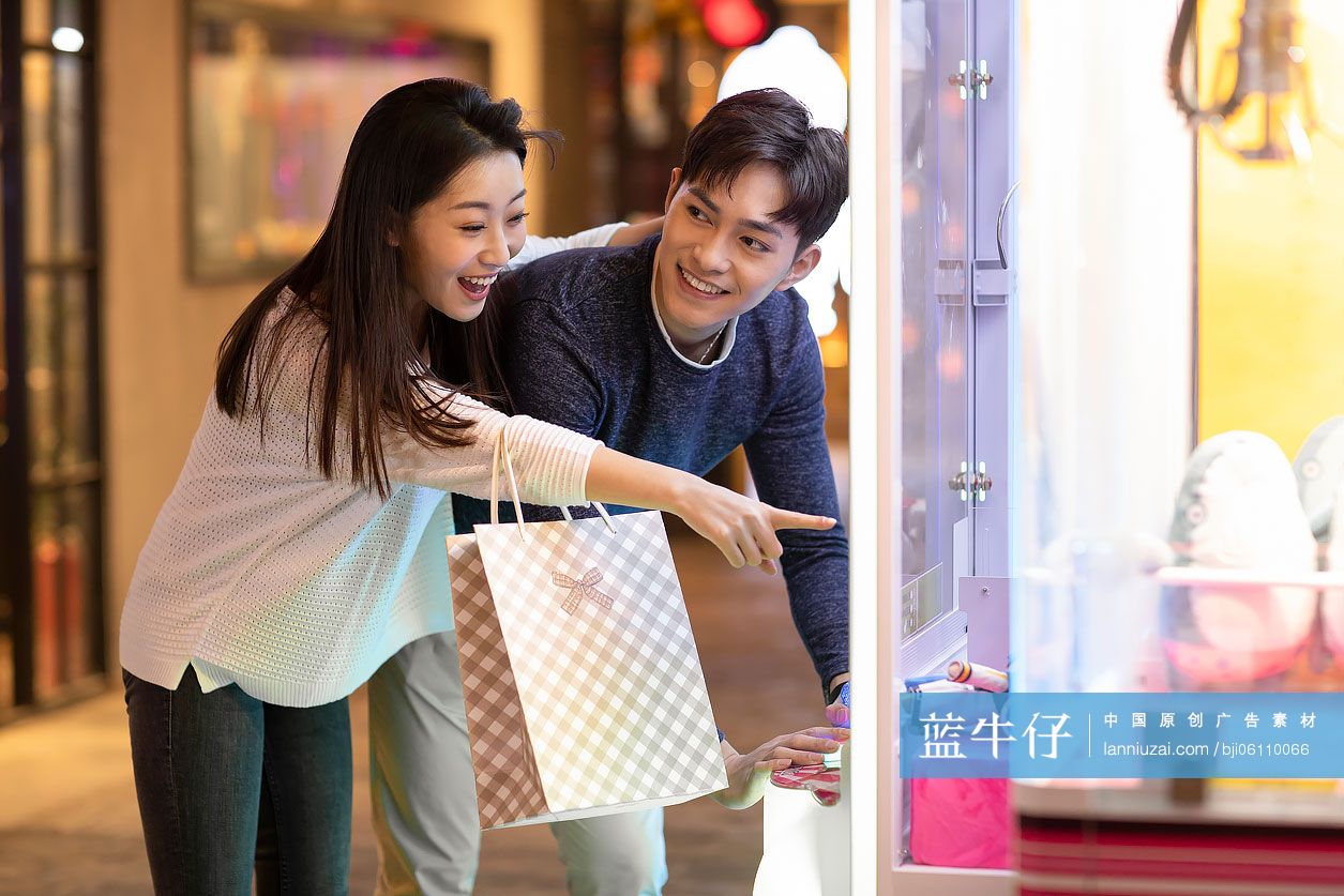 快乐的年轻情侣在商场玩抓娃娃机游戏