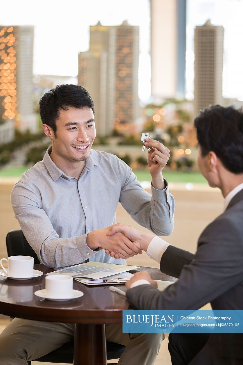 Happy young Chinese man buying new house from realtor