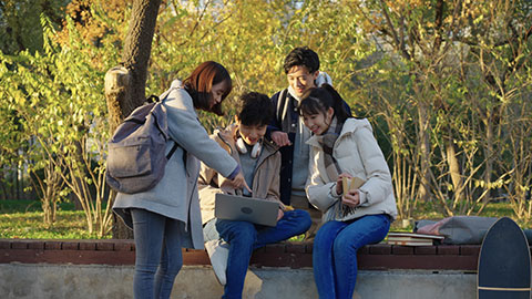 Happy Chinese college students using laptop and discussing