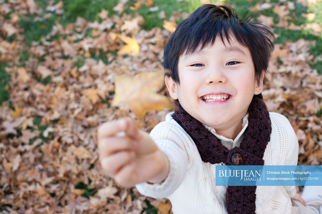 Chinese boy holding up a leaf in autumn