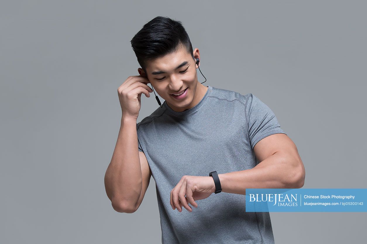 Young Chinese male athlete with headphones checking smart watch after exercising