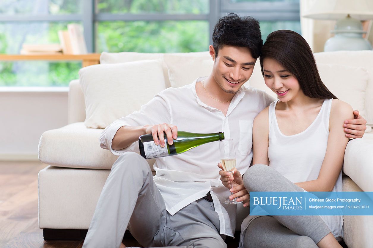 Cheerful young Chinese couple drinking champagne in living room