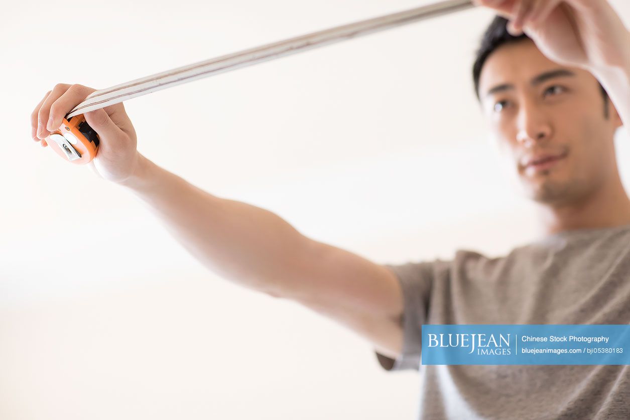 Young Chinese man measuring wall