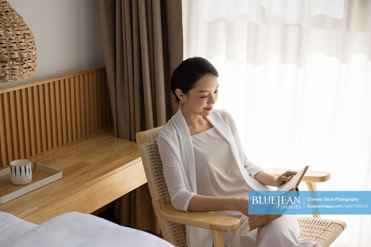 Elegant young Chinese woman reading book at home