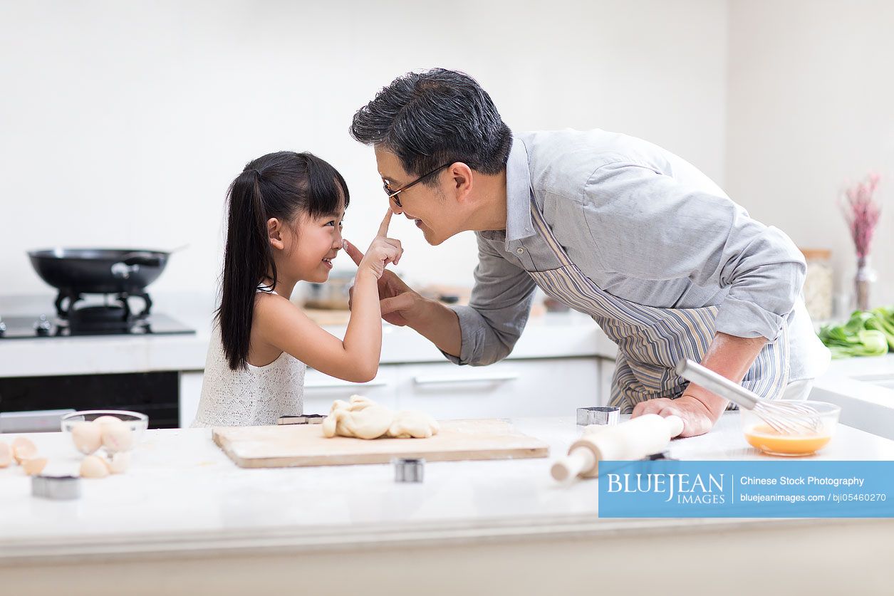 Happy little Chinese girl and grandfather baking cookies in kitchen