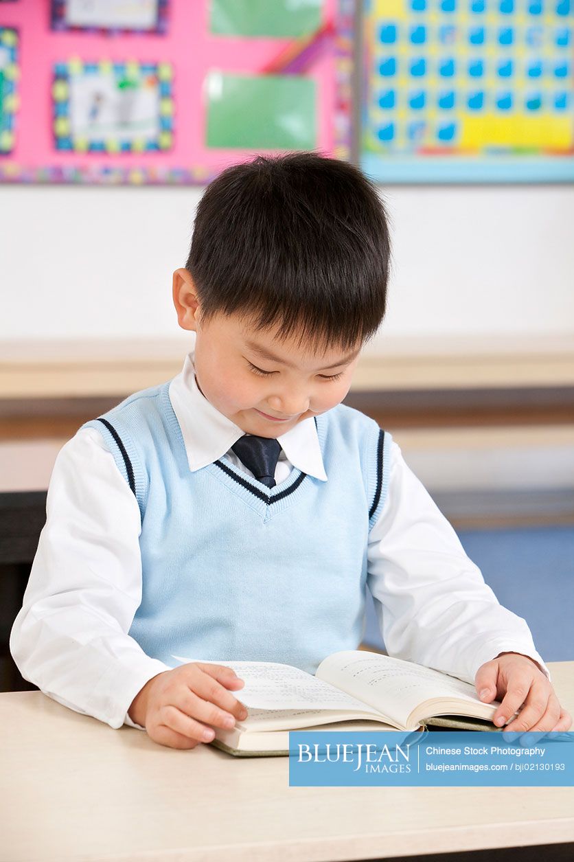 Young Chinese boy reading at his desk in a classroom