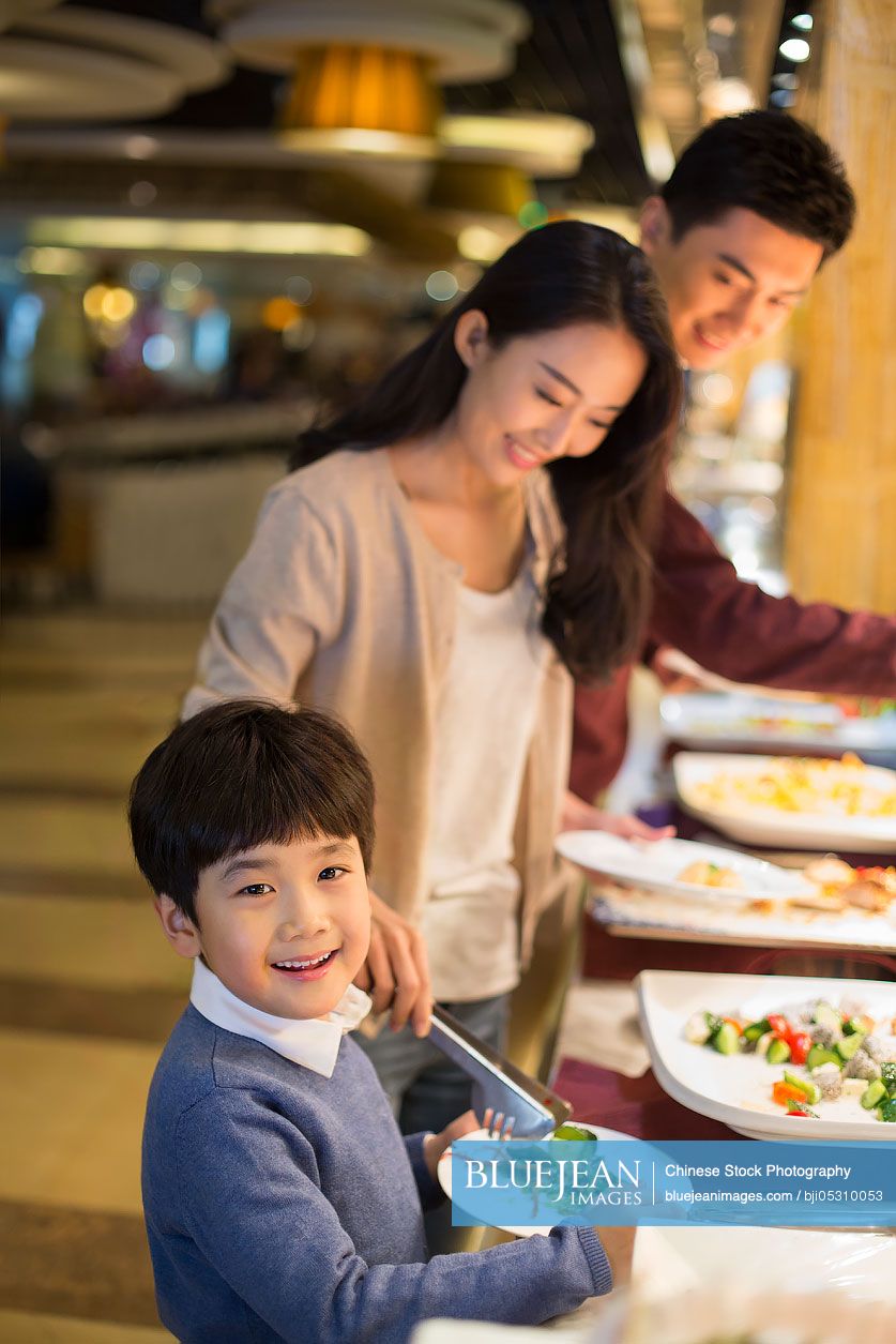 Cheerful young Chinese family taking food from buffet table