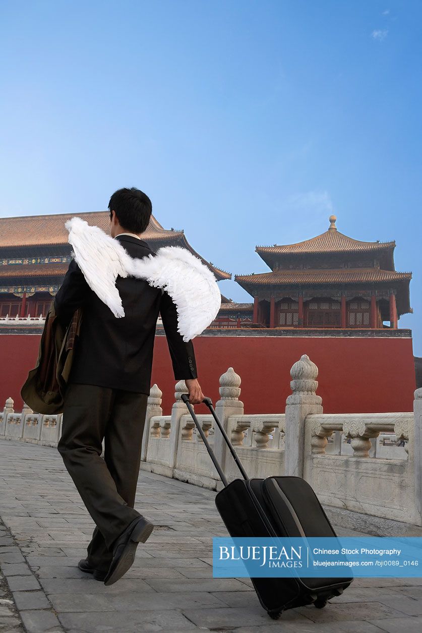 Chinese Man Wearing White Wings, Pulling A Suitcase