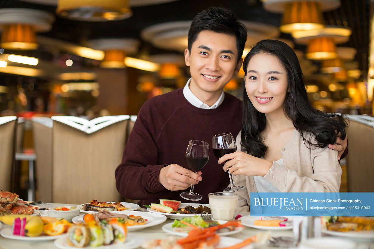 Cheerful young Chinese couple toasting with red wine