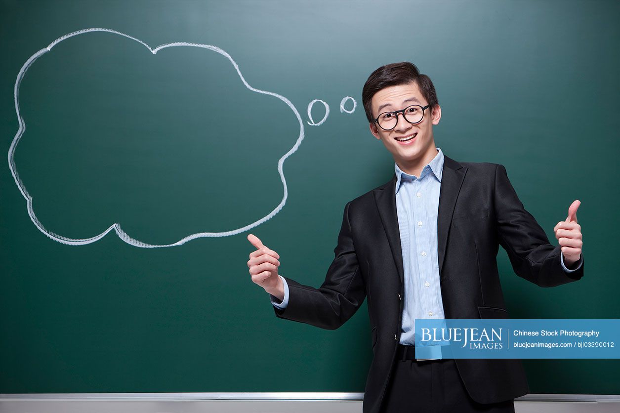 Humorous male Chinese teacher doing thumbs up in classroom