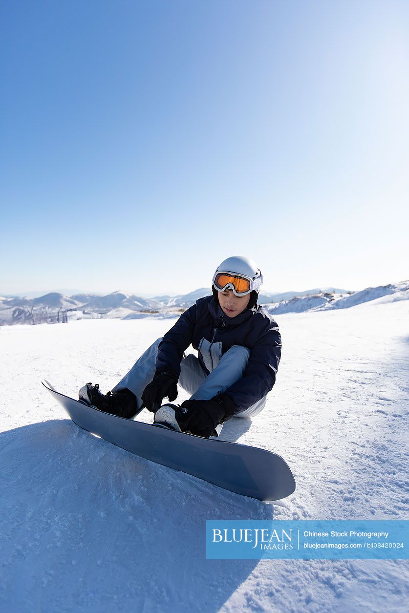 Young Chinese man with snowboard on the snow