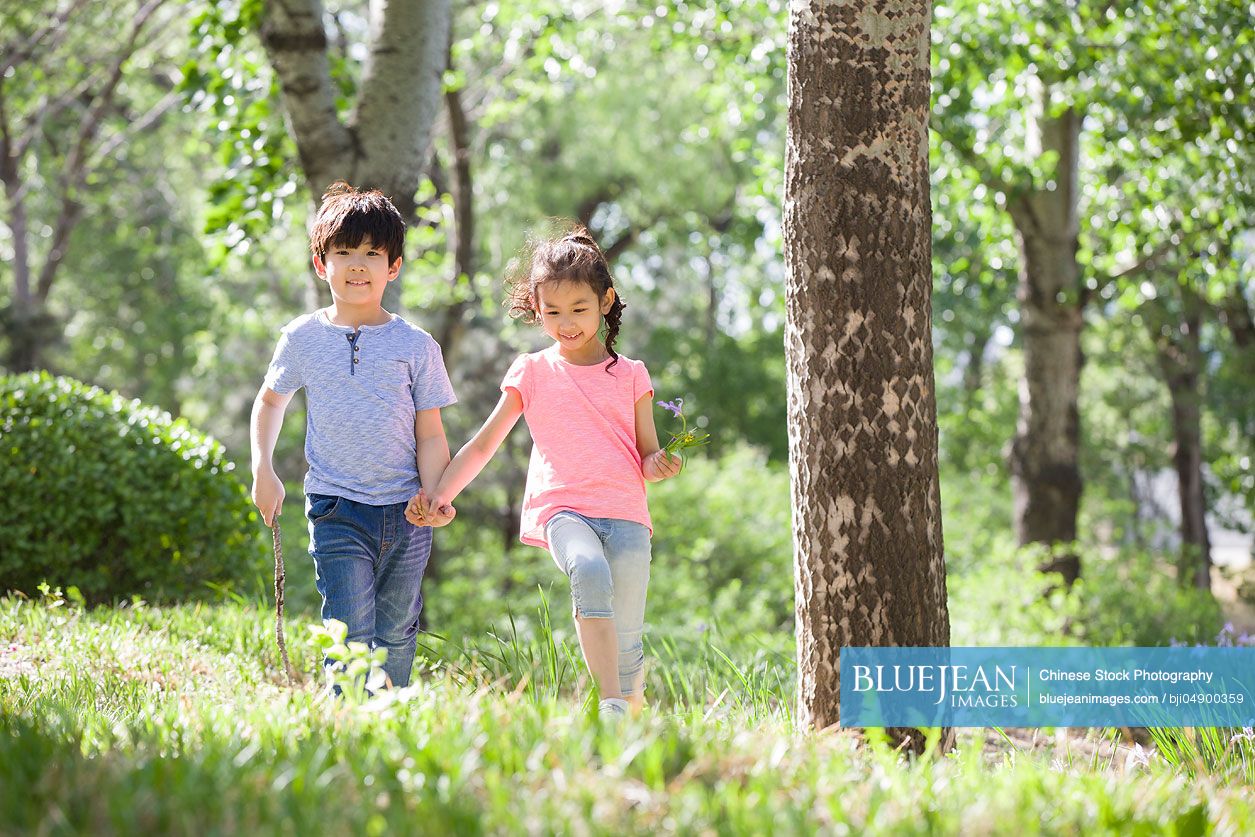 Happy Chinese children holding hands walking in woods