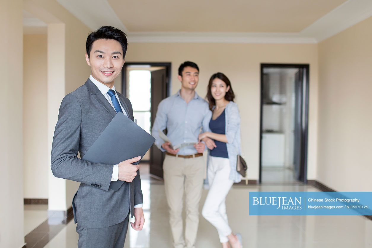 Confident Chinese realtor and young couple in new house