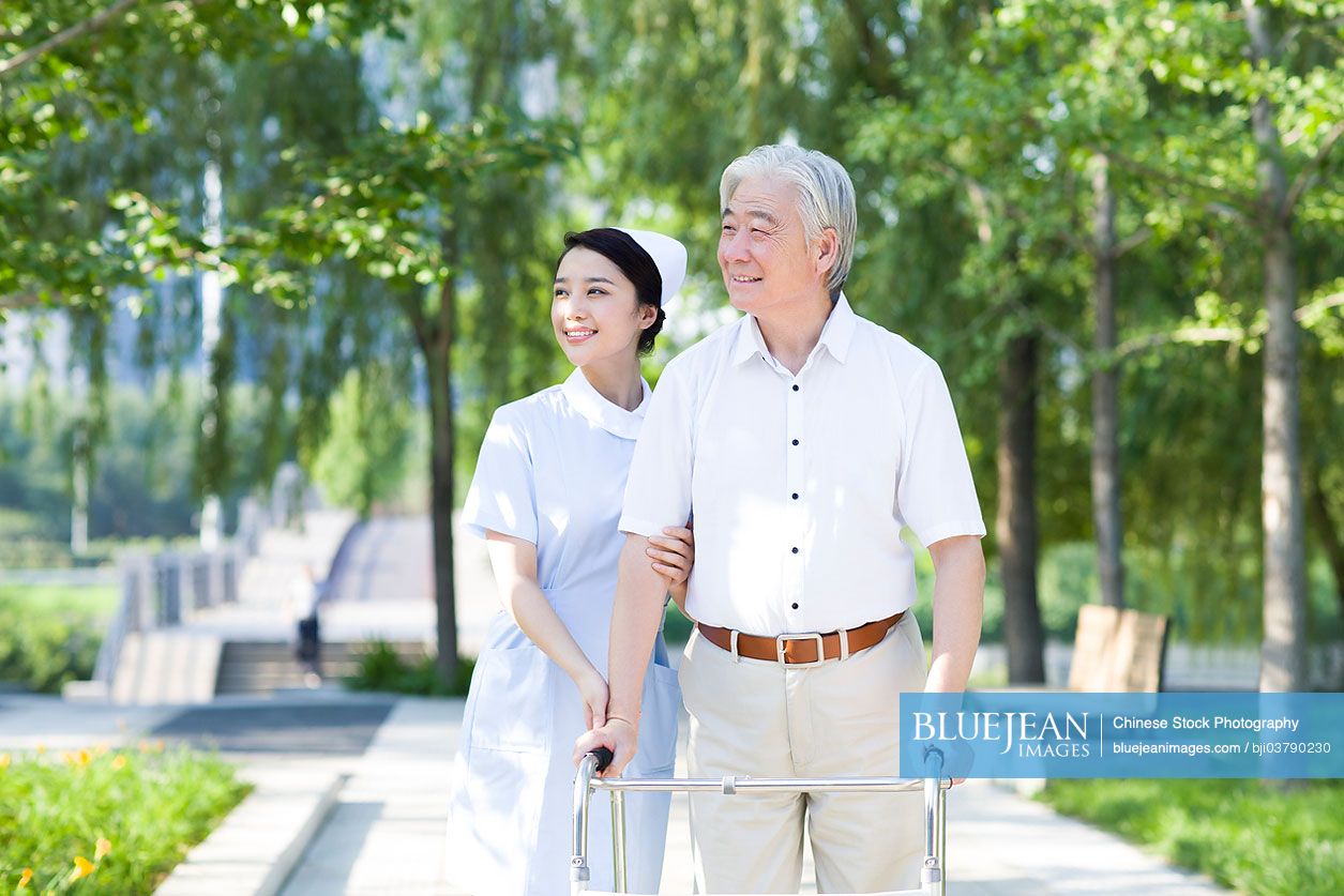 Senior Chinese man walking with walking frame under nurse's assistance