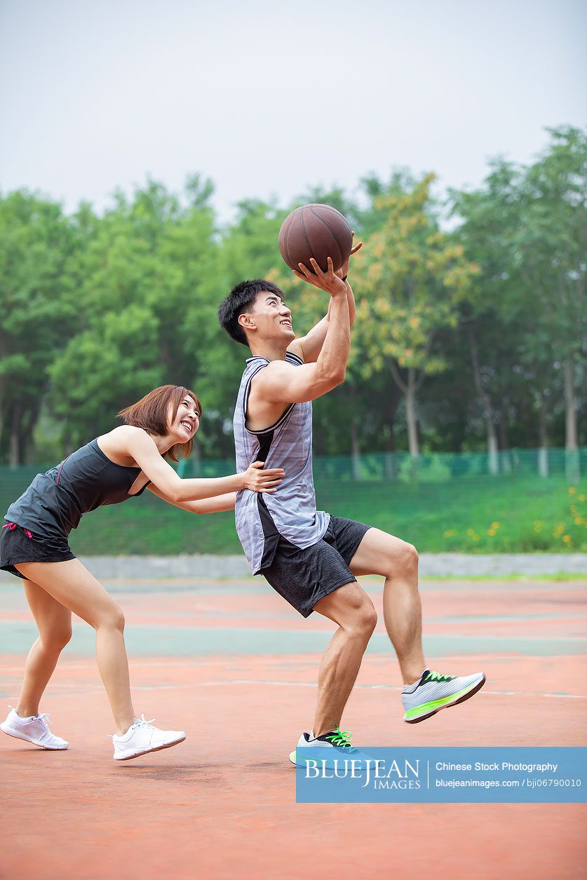 Happy young Chinese couple playing basketball outdoors