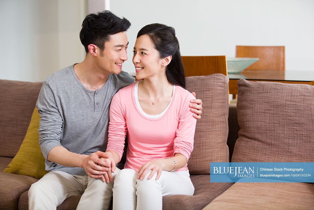 Happy young Chinese couple sitting on sofa