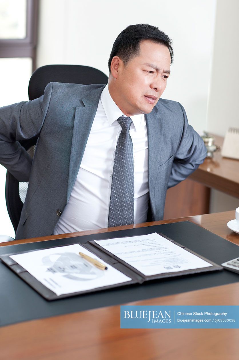 Mature Chinese businessman suffering from back pain in office