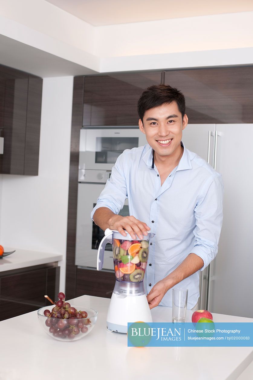 Chinese man making fresh fruit juice in kitchen