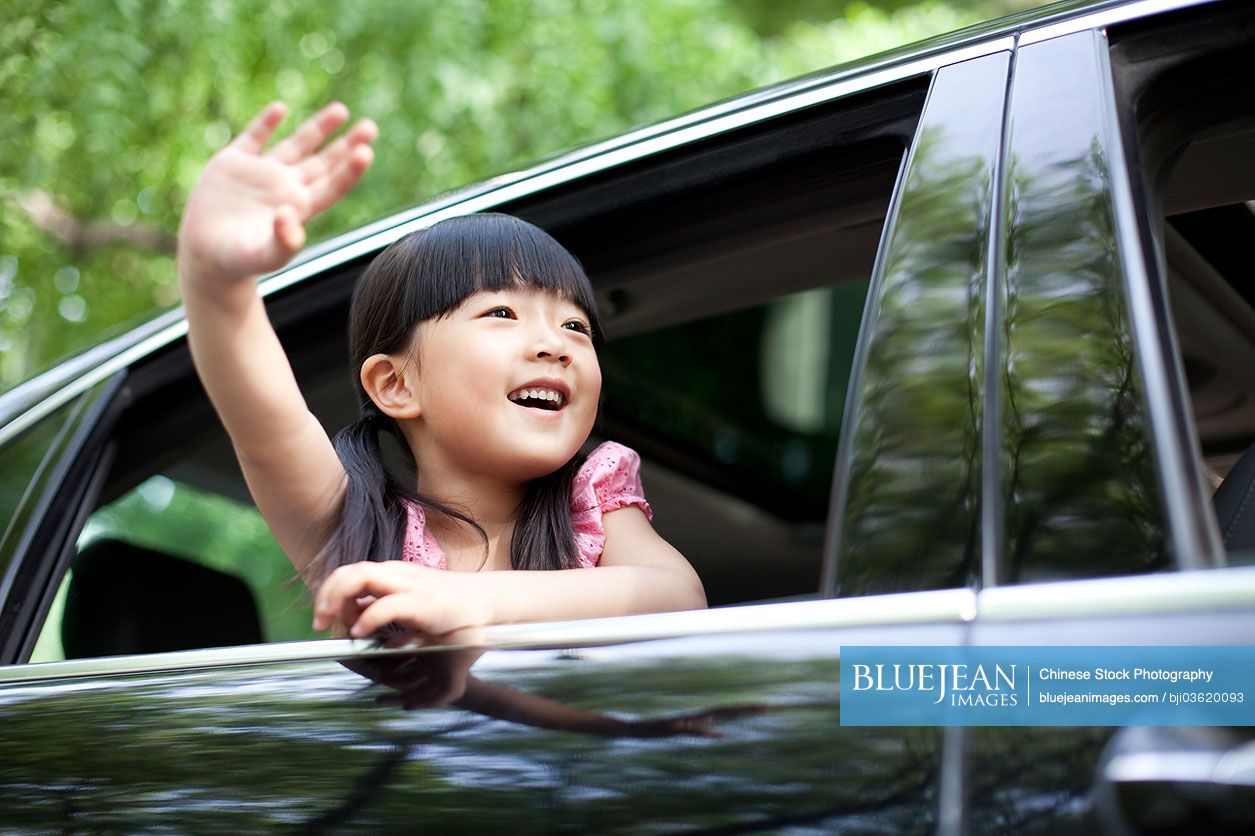 Cheerful Chinese girl waving out of car window