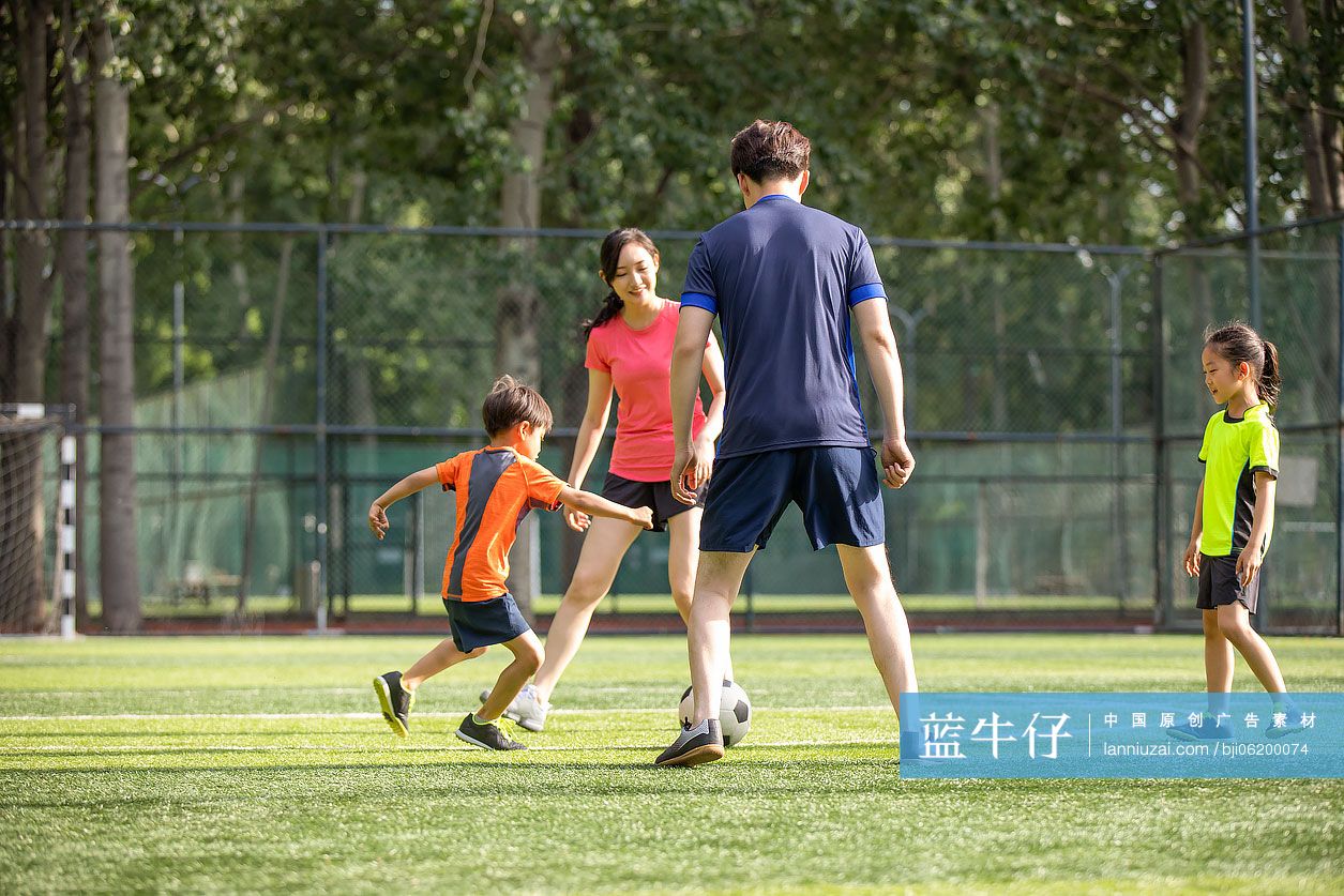 快乐的年轻家庭在足球场踢足球