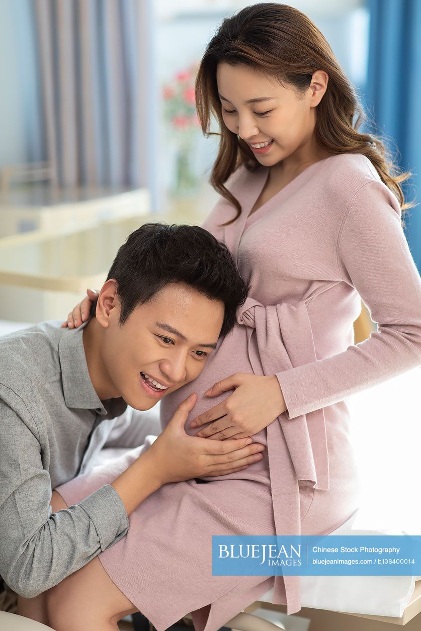 Chinese husband listening to his pregnant wife's belly in hospital ward