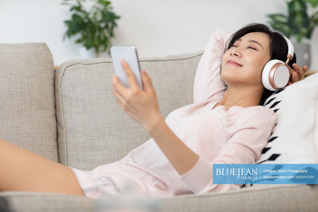Happy young Chinese woman wearing headphones on sofa
