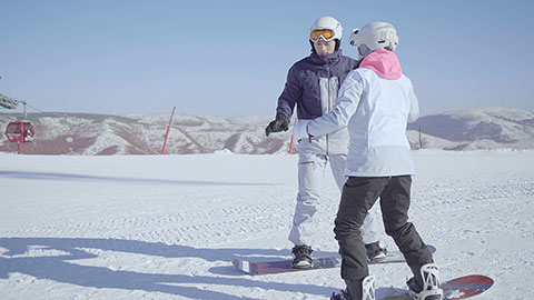年轻男子教女朋友单板滑雪