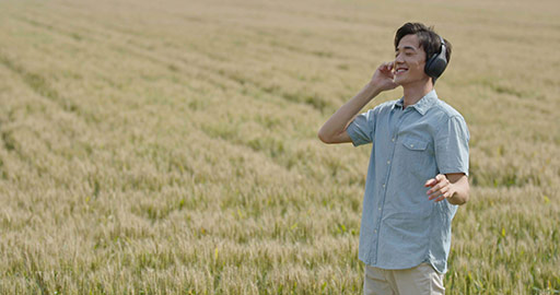 Happy young Chinese man wearing headphones in wheat field,4K