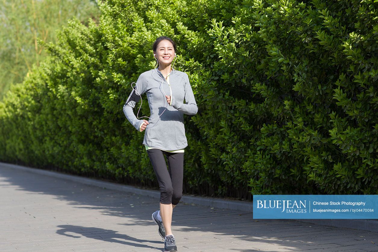 happy-mature-chinese-woman-running-and-listening-to-music-in-park-high