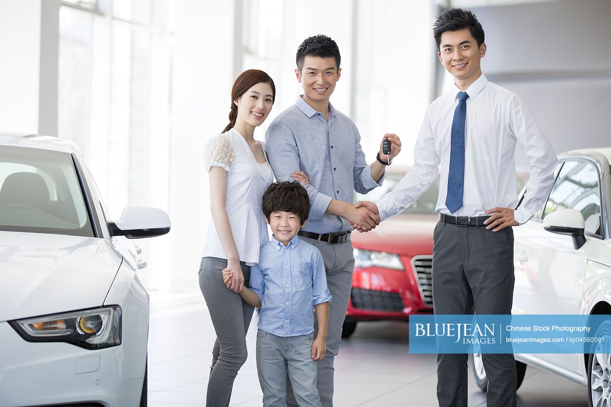 Young Chinese family buying car in showroom