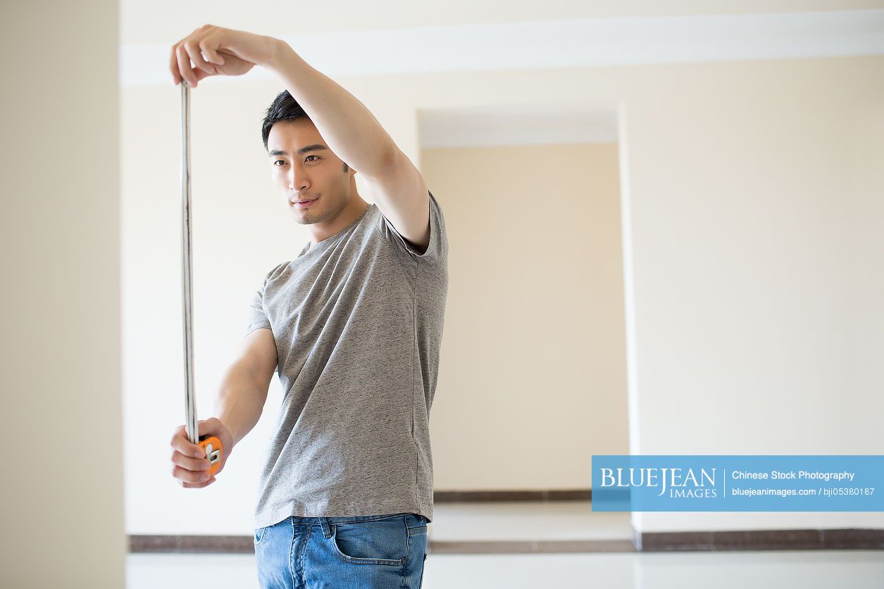 Young Chinese man measuring wall